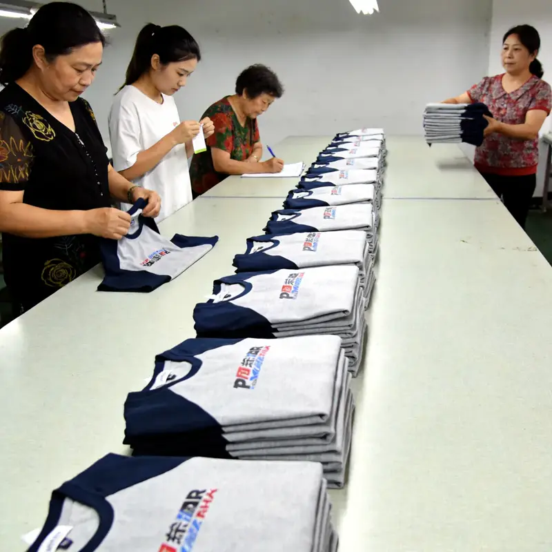 Quality control inspector checking a finished sublimated esports jersey on a white inspection table with rulers, color-control charts, and a finished sample pinned to the wall in the background